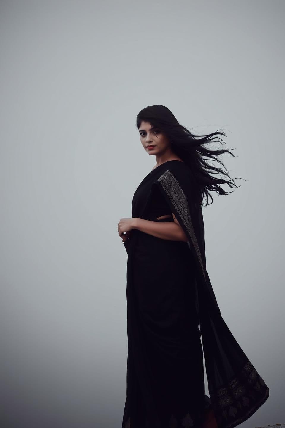 AI generated: IMPORTANT: Generate with all text in BN script only. Ayesha slowly walks from a distance,
wearing a black sari, her hair flowing in the wind.
Her eyes are red—she may have been cry